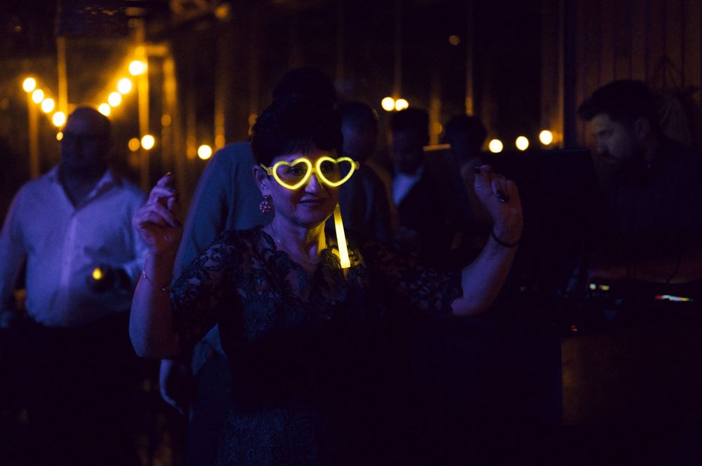 Woman wearing glowing heart-shaped glasses at a dark party venue with bokeh lights in the background.