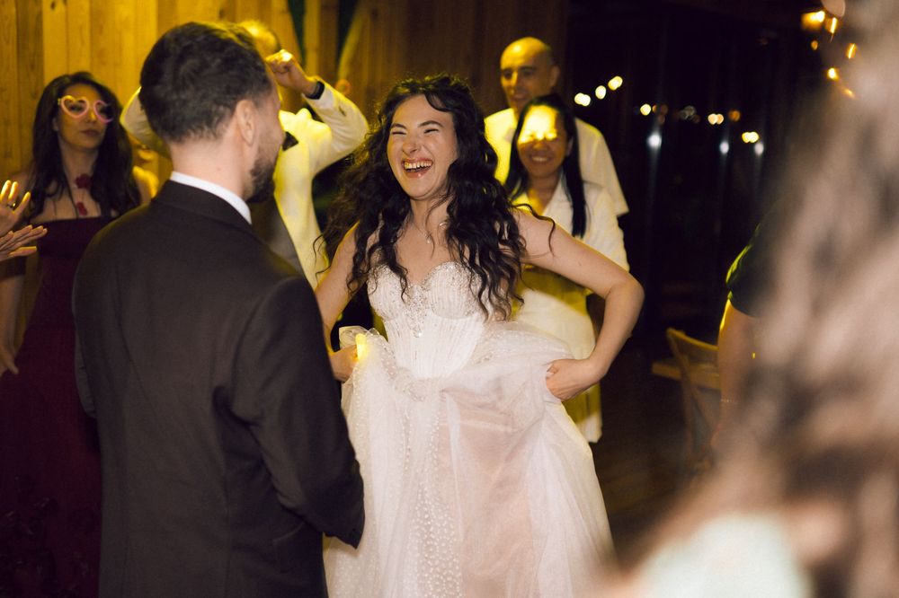 Bride in white tulle gown laughing joyfully while dancing with guests at elegant wedding reception.