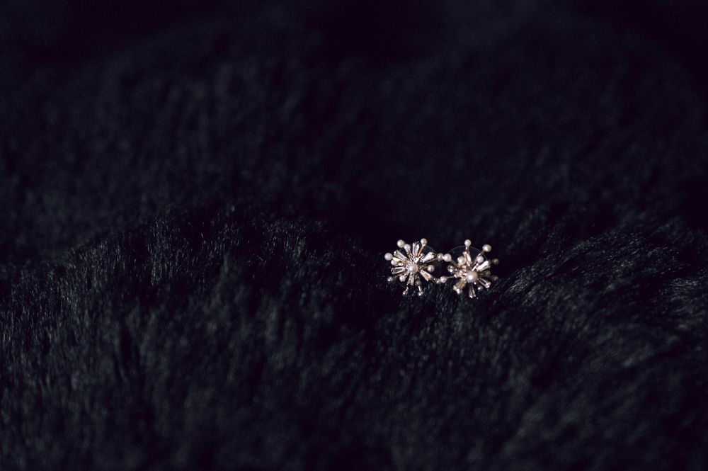 Delicate silver snowflake stud earrings displayed on a dark black fur background.