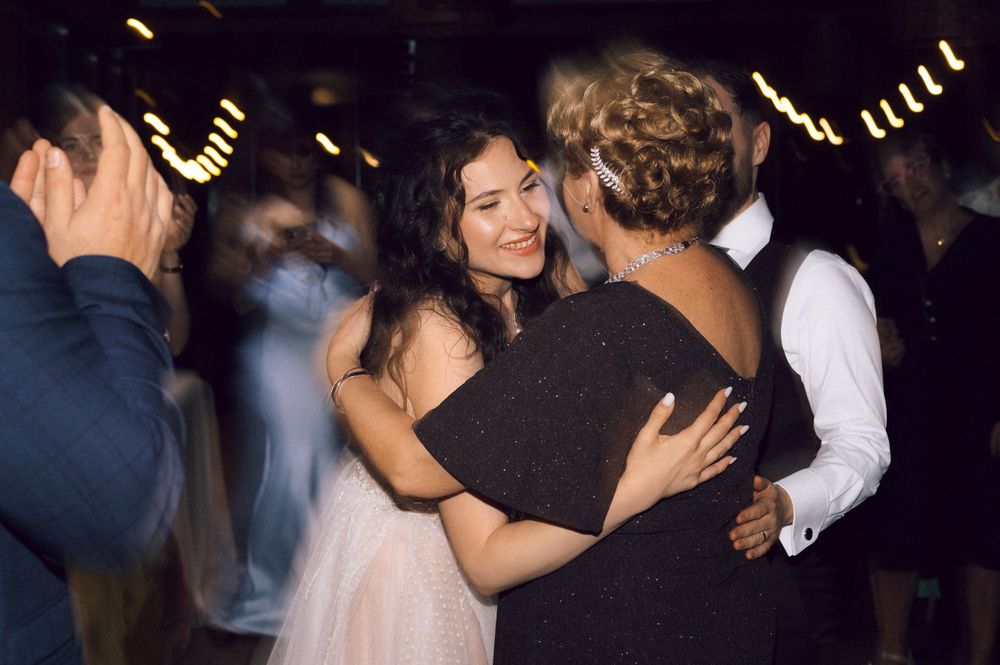 Guests dancing and embracing at an elegant wedding reception in a dimly lit venue with string lights.