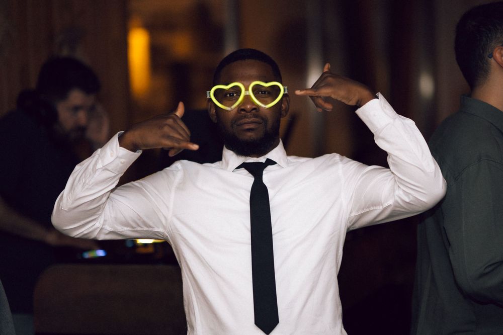 Man in white shirt and black tie wearing yellow heart-shaped sunglasses at a party.