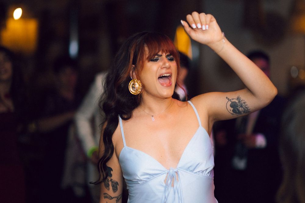 Woman with tattoos and gold earrings dancing joyfully in a white dress at a party.