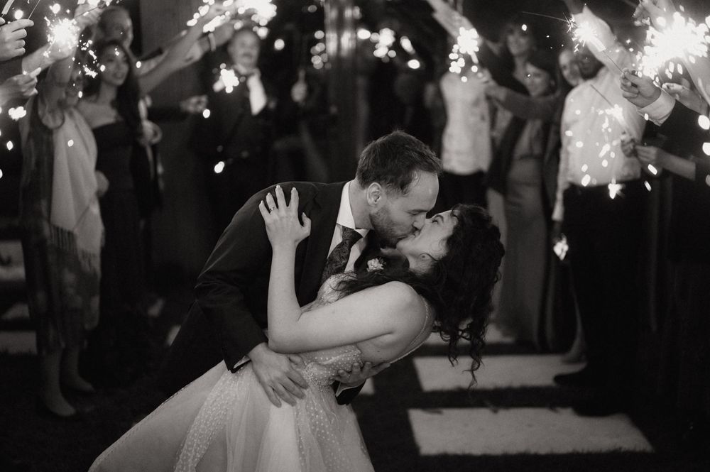 Black and white photo of bride and groom sharing a romantic dip kiss surrounded by sparklers at their wedding reception.