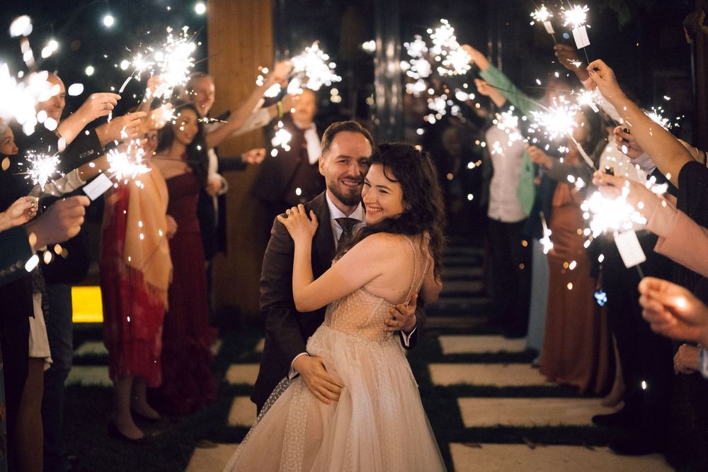 Newlywed couple embracing during sparkler exit at night wedding celebration with guests holding sparklers.