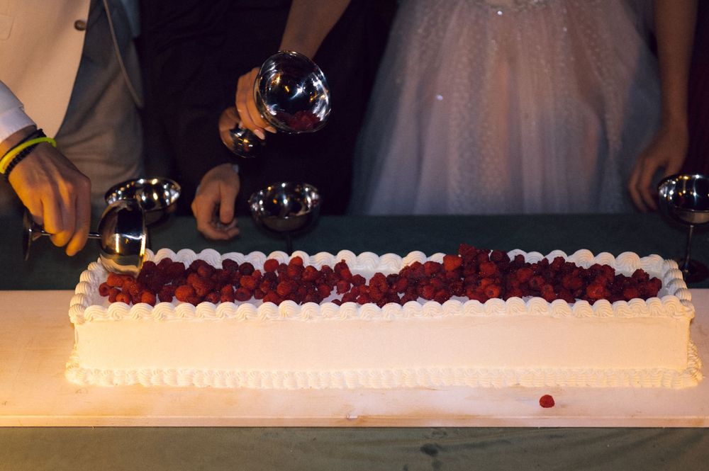 Elegant wedding cake topped with fresh raspberries and whipped cream frosting being served at a reception.