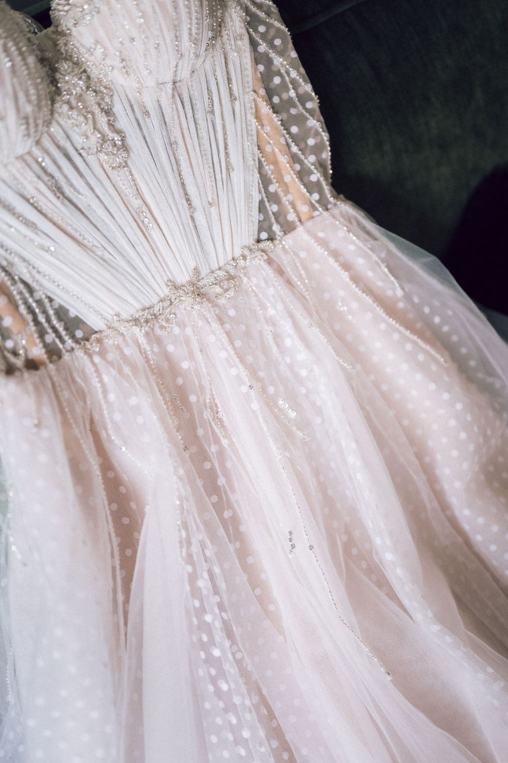 Elegant blush pink wedding gown with delicate polka dot tulle skirt and pearl-embellished bodice displayed on hanger.