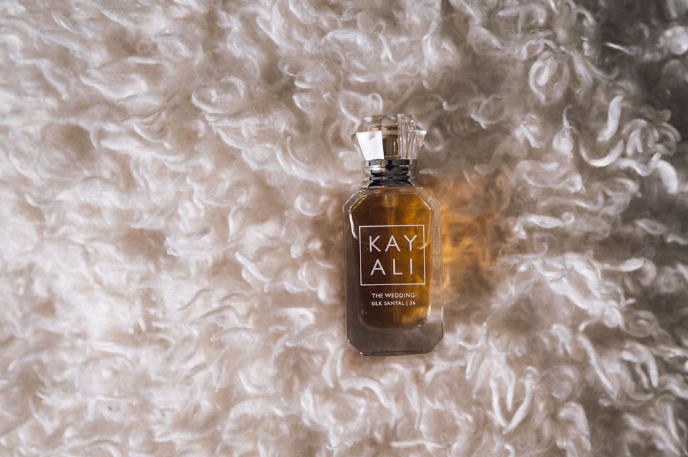 Kayali perfume bottle in amber glass resting on soft white fluffy fur texture background.