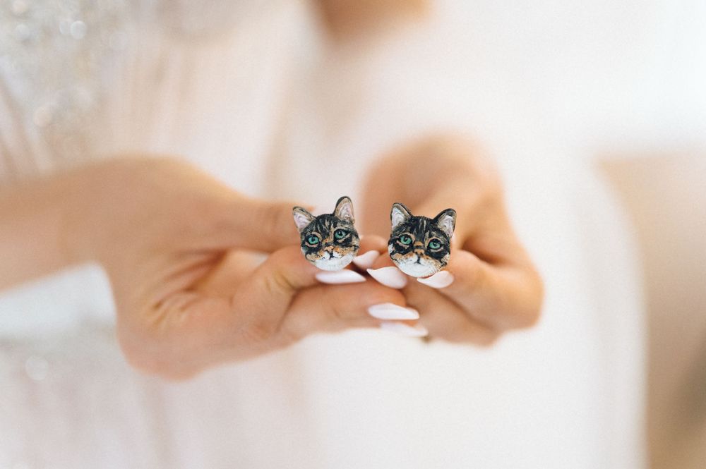 Bride holding cute black cat face stud earrings with white accents, showcasing unique feline jewelry for weddings.