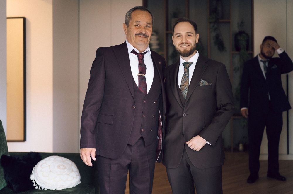 Two men in elegant suits posing together at a formal Jewish event, with a kippah visible on a table nearby.