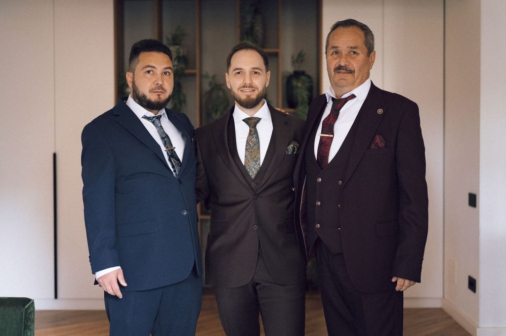 Three well-dressed men in formal suits posing together for a portrait photo indoors.