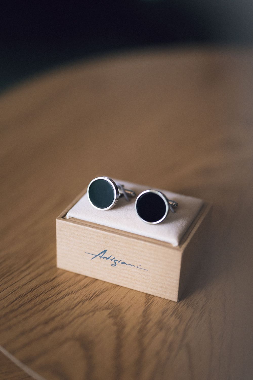 Elegant round silver cufflinks with dark enamel centers displayed on an Artigiani branded gift box on a wooden surface.