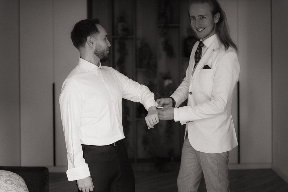 Two men in formal white shirts shake hands indoors in a black and white photo.