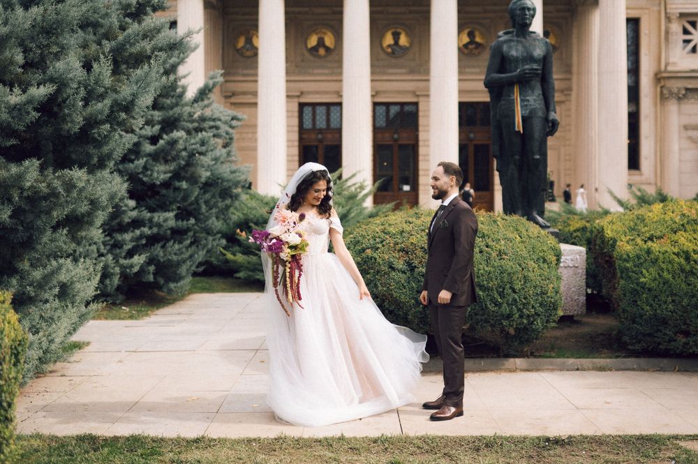 Bride and groom posing in front of a grand building with columns and statue on their wedding day.