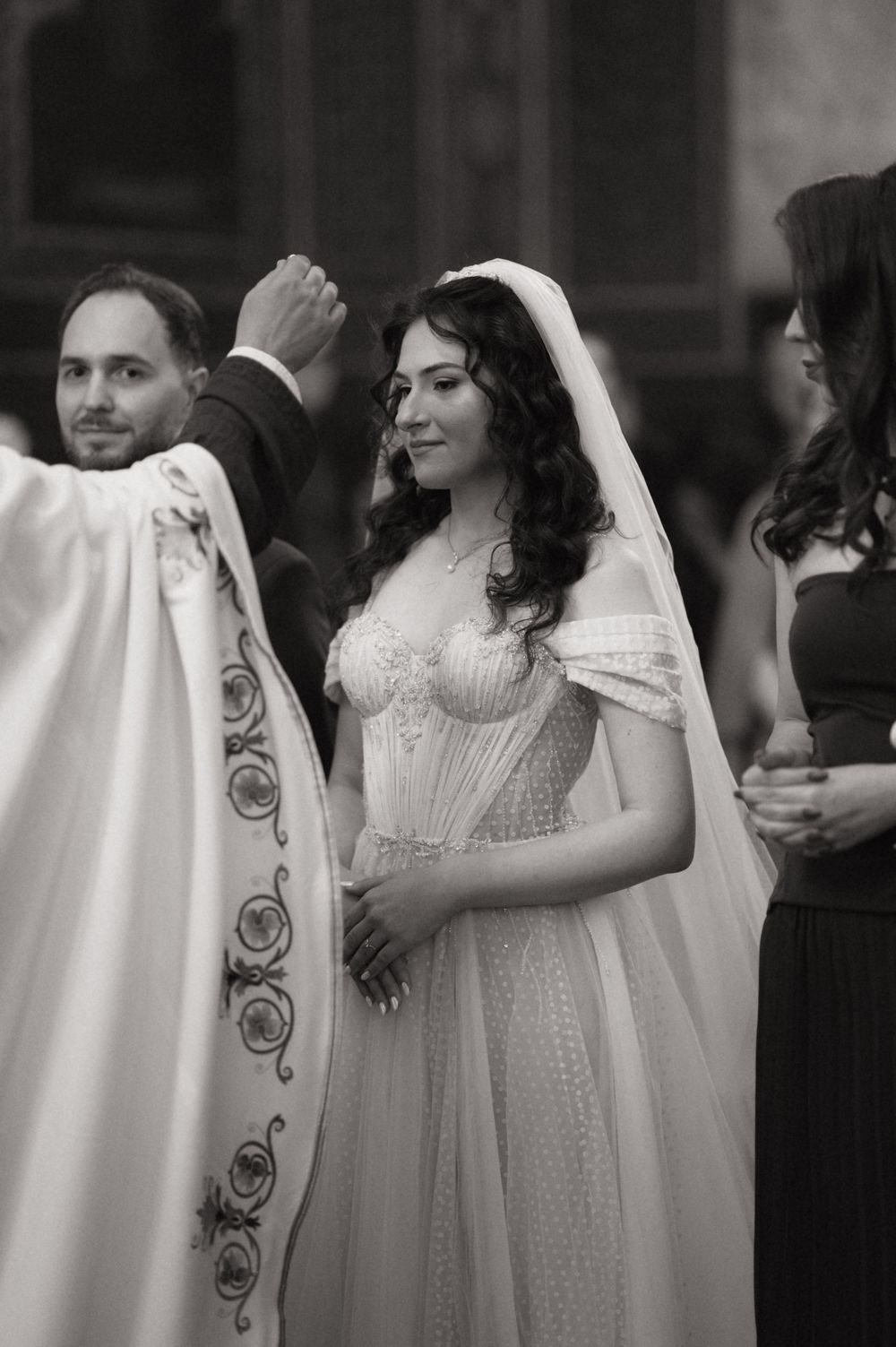 Black and white photo of a bride in a white gown and veil smiling during a wedding ceremony.