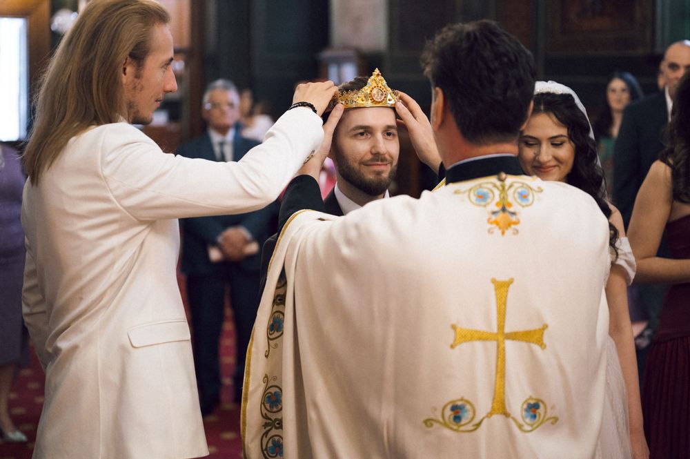 A man receives a crown during a religious ceremony, with clergy in white robes and a cross present.