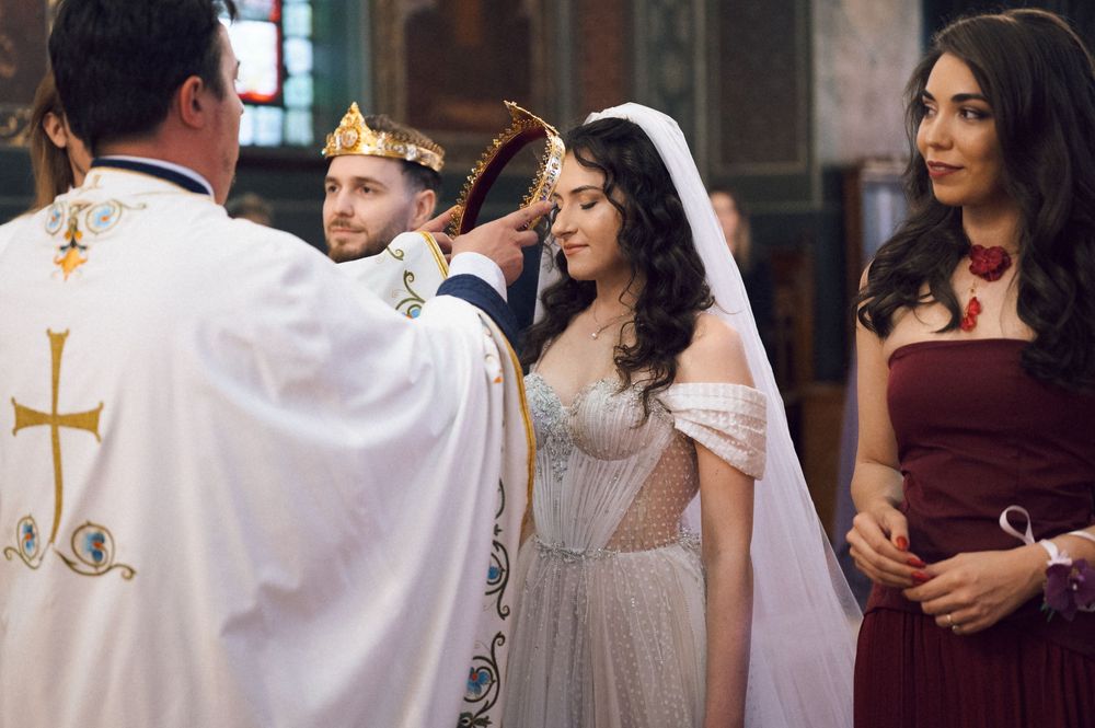 Orthodox Christian wedding ceremony with priest placing crown on bride, groom and bridesmaid in church.