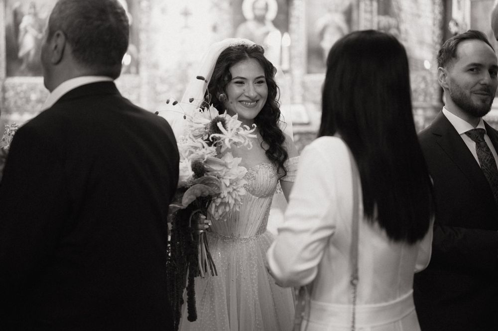 Black and white wedding photo of smiling bride holding white flowers bouquet inside a church ceremony.