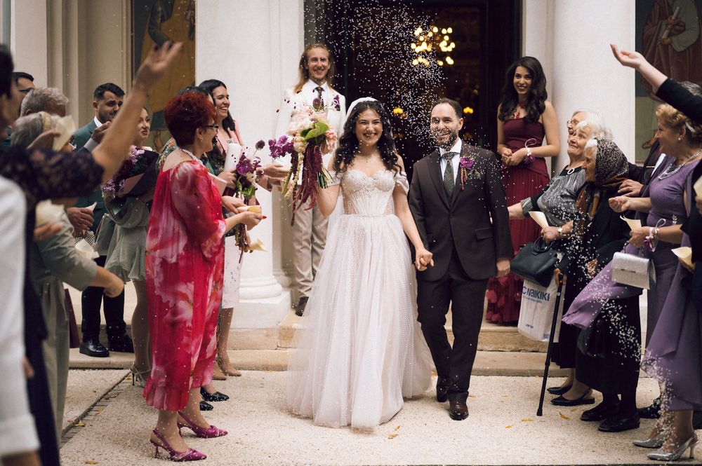 Bride and groom walk down aisle as guests toss confetti at elegant wedding ceremony.