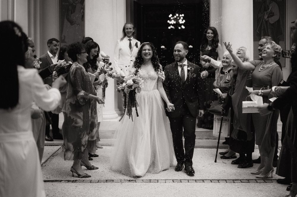 Black and white photo of a smiling bride and groom walking through cheering guests after their wedding ceremony.