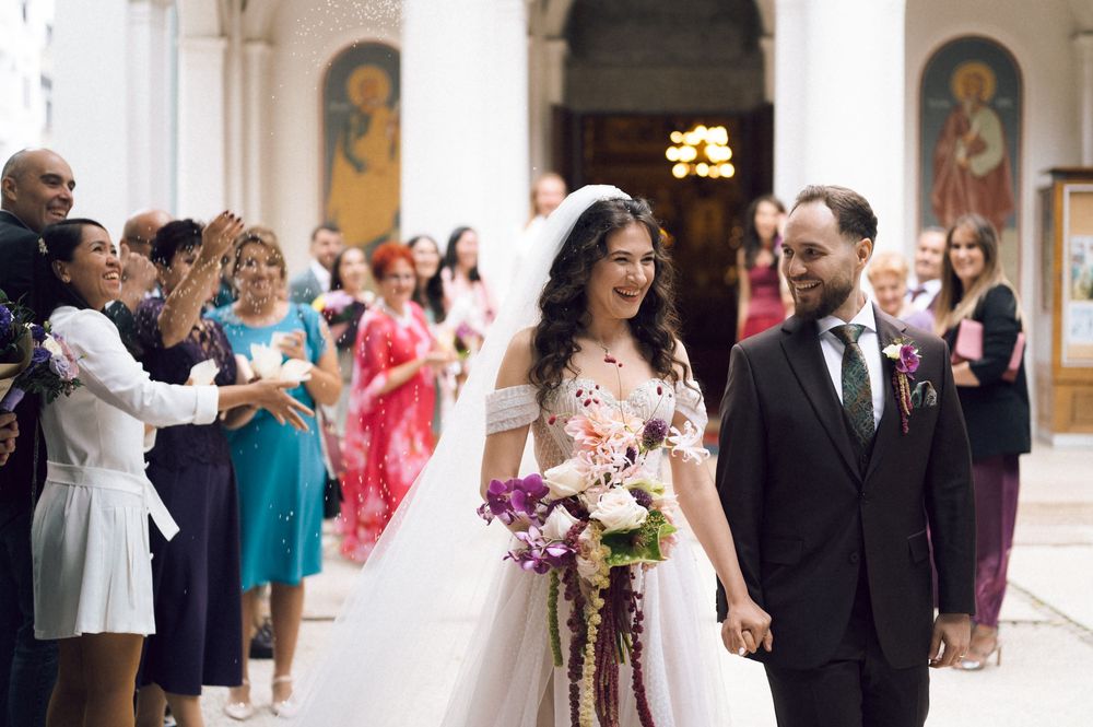 Bride and groom walk down church aisle after wedding ceremony, guests applauding, bride holding colorful bouquet.