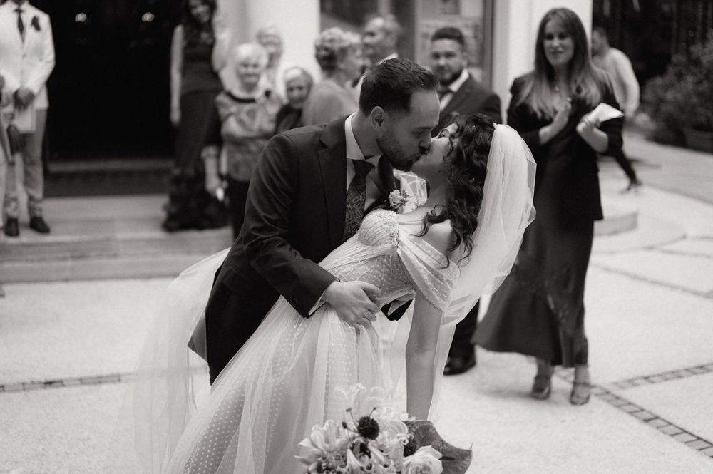 Black and white photo of a bride and groom sharing a first kiss at their outdoor wedding ceremony.