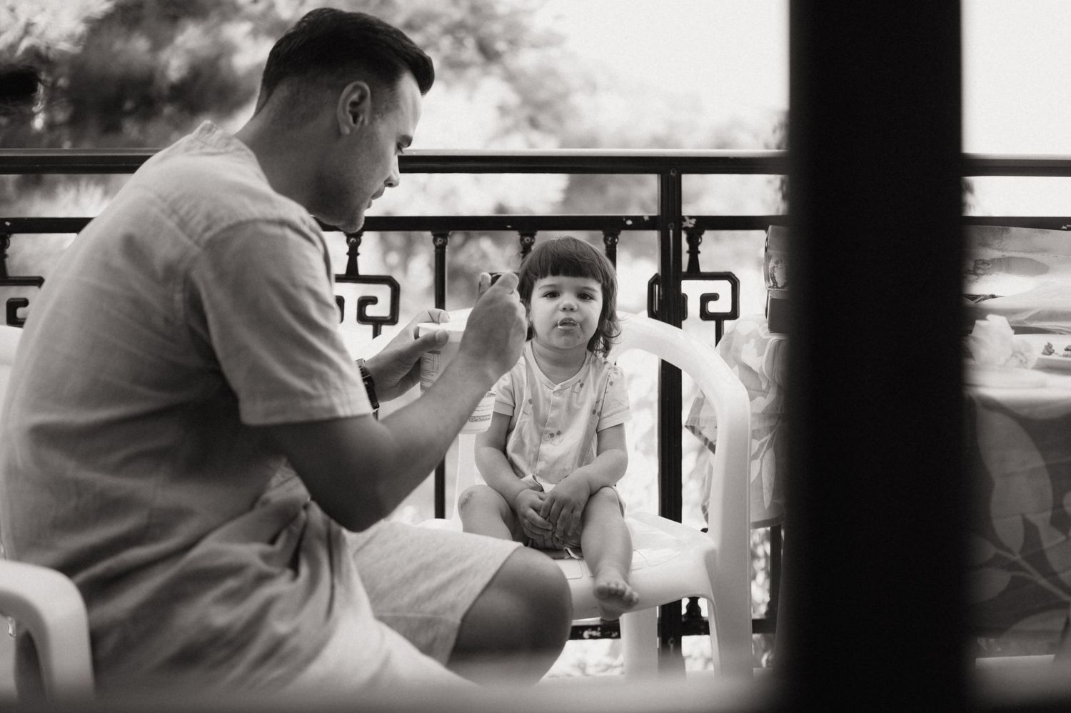 Black and white photo of a father talking to his young daughter on a balcony.