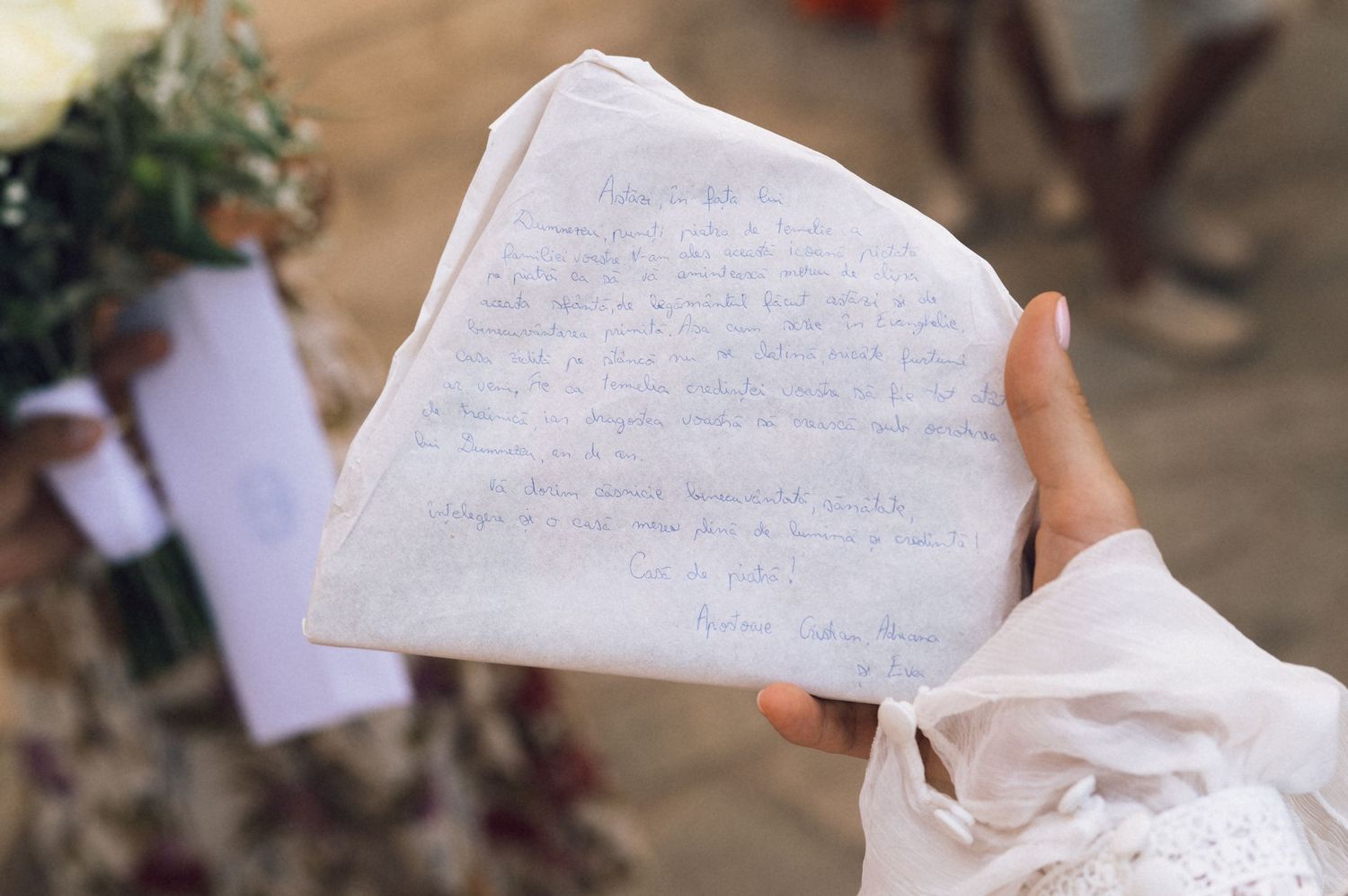 Person holding handwritten wedding vows on white fabric at an outdoor ceremony with flowers in background.