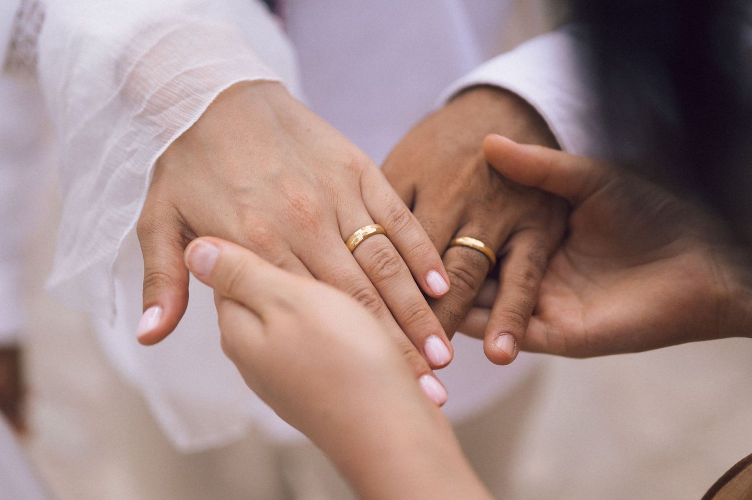 Close-up of interracial couple exchanging gold wedding rings during marriage ceremony.