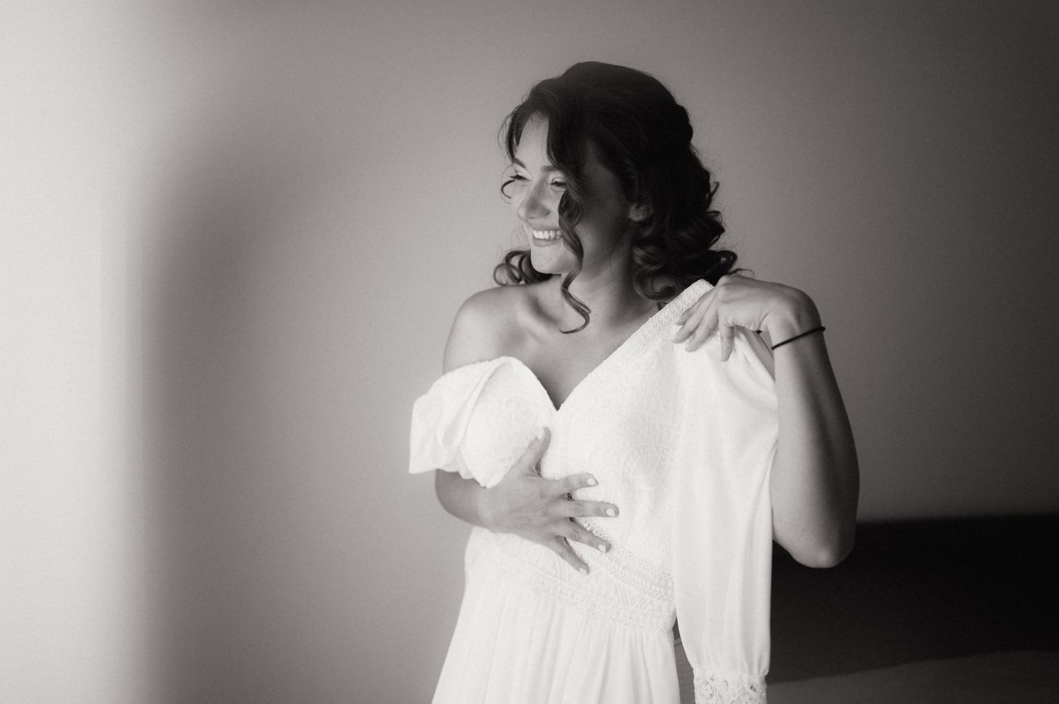 Elegant bride in white off-shoulder gown poses gracefully in black and white portrait photography.
