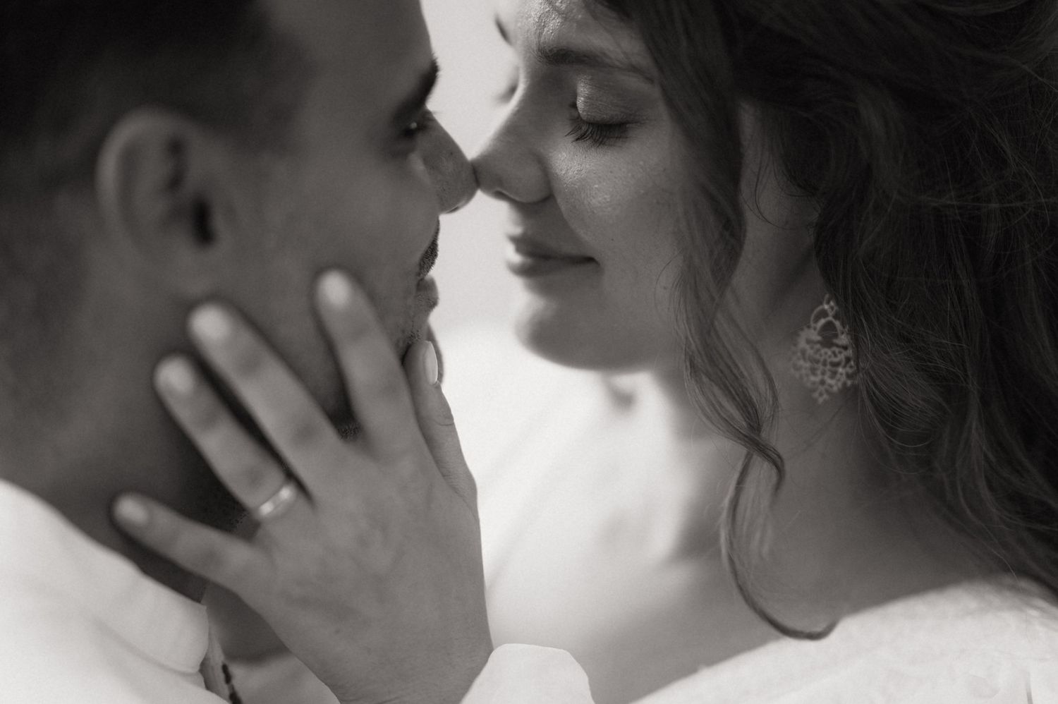 Black and white romantic close-up of a couple nearly kissing, bride wearing chandelier earring and groom with wedding band.