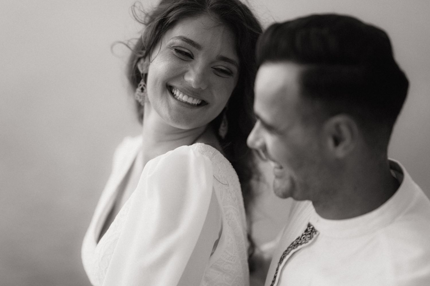 Black and white photo of a smiling woman in white dress sharing a joyful moment with a man.