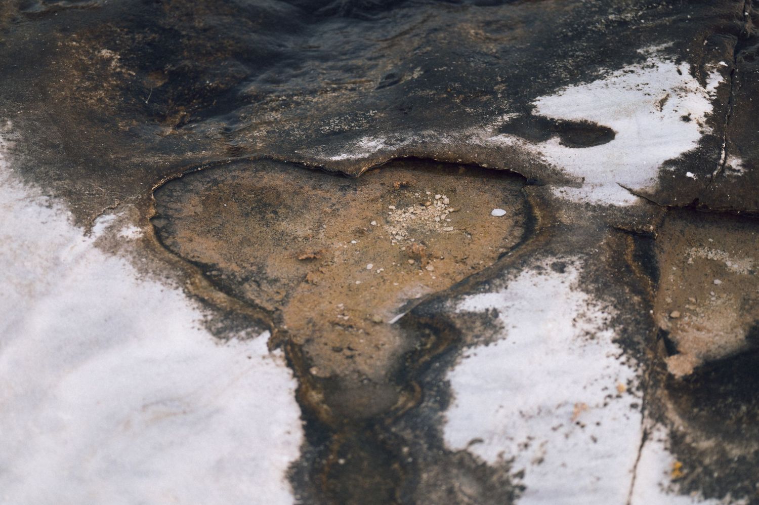 Aerial view of melting snow and ice revealing dark wet ground with a heart-shaped mud formation in winter landscape.