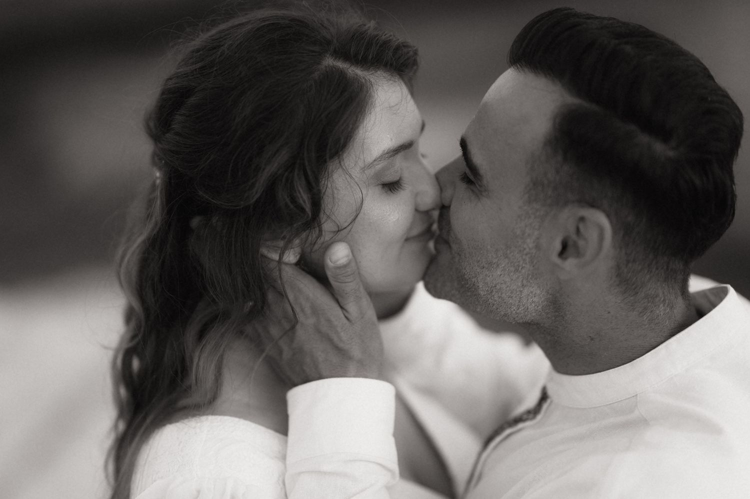 Black and white photo of a romantic couple sharing a tender kiss, man gently holding womans face.