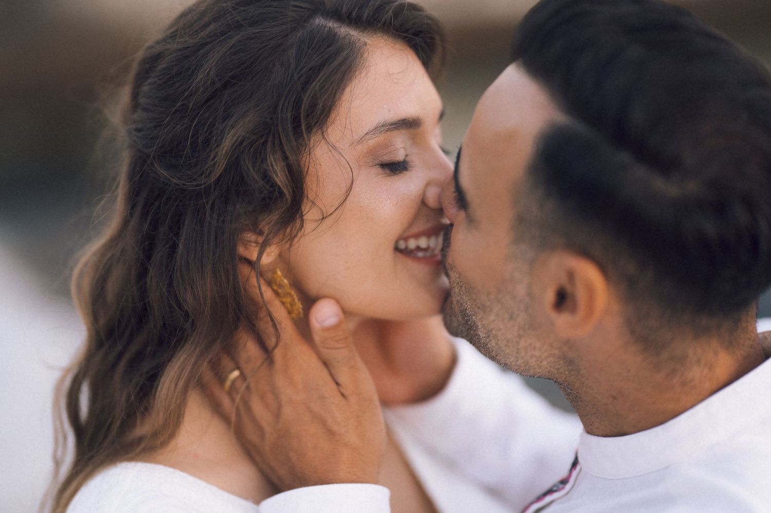 Romantic couple sharing a tender kiss, man gently holding woman's face, both dressed in white.