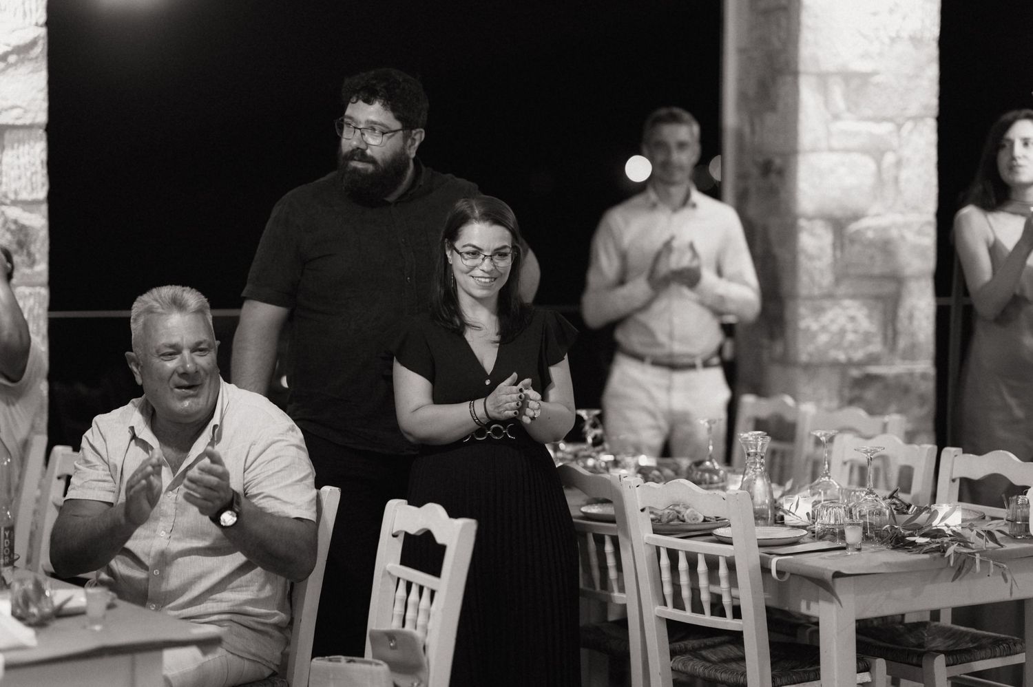 Black and white photo of guests gathered at an outdoor evening dinner party, with a couple standing together in the center.