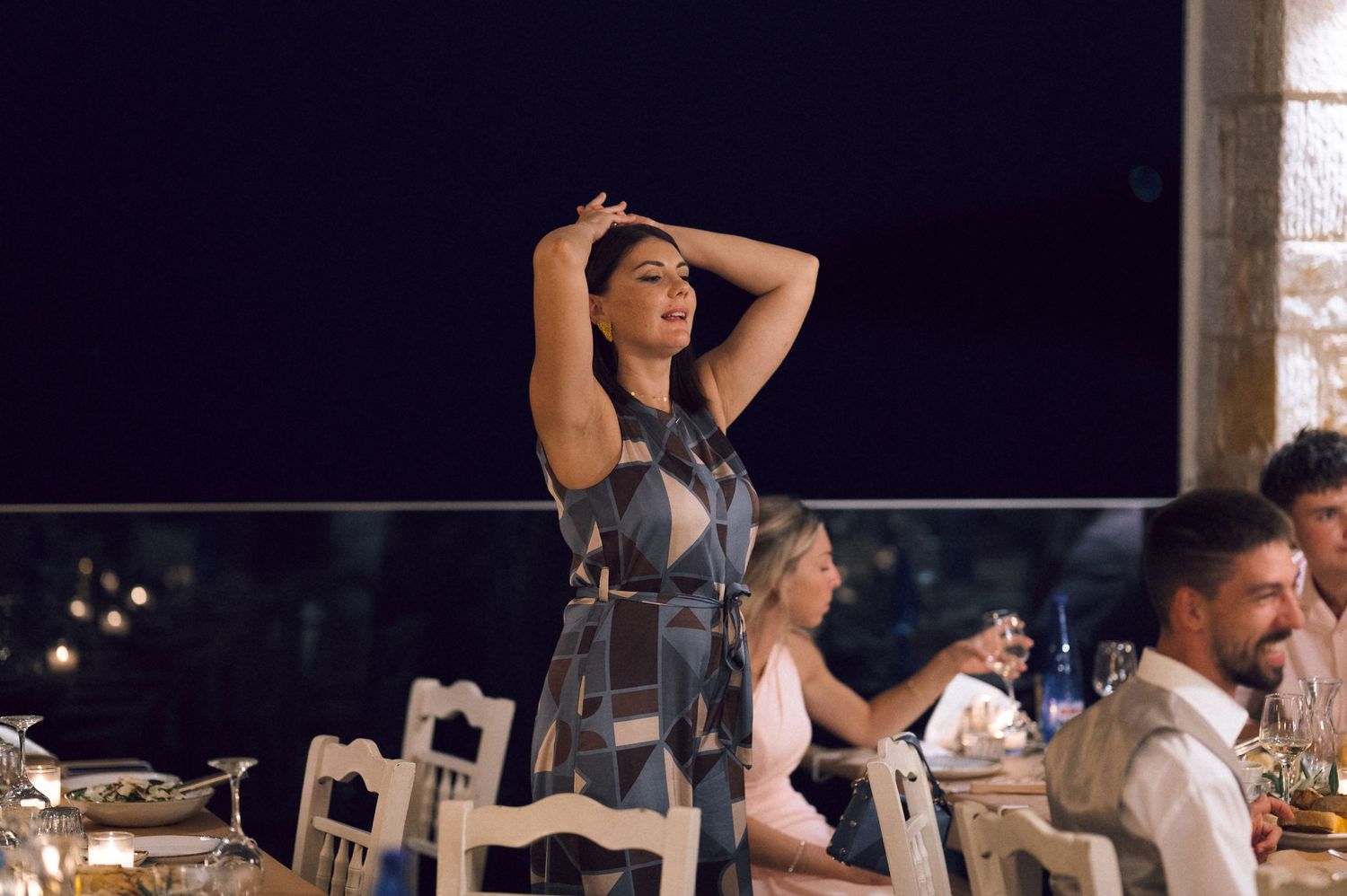 Woman in blue dress dancing at an outdoor evening dinner party with guests seated at tables.
