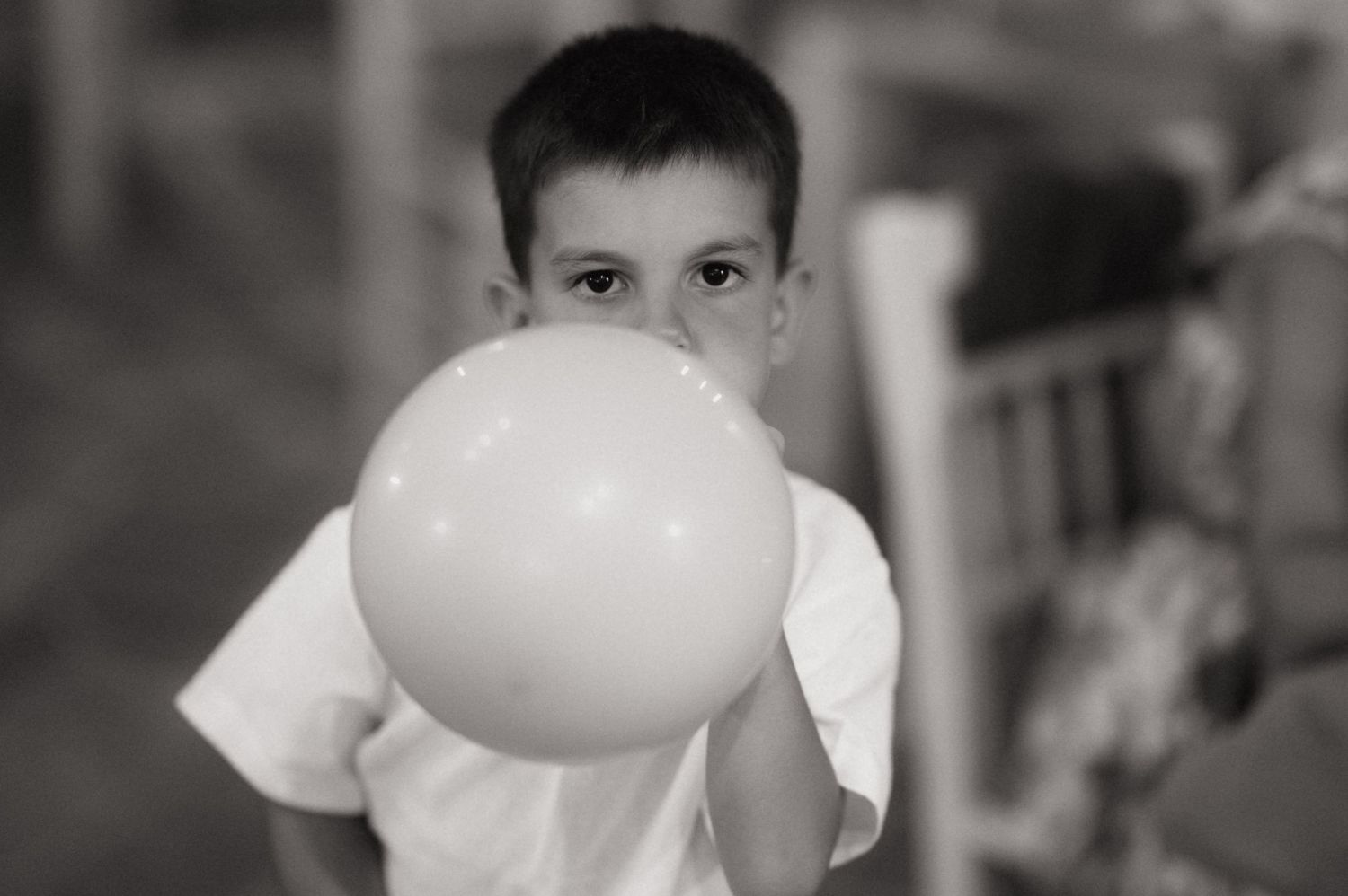 Black and white photo of a young boy blowing up a balloon at a party.