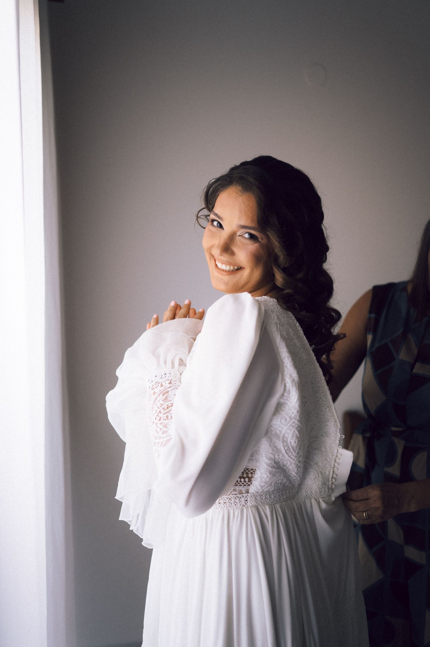 Smiling bride in white lace wedding dress looking over shoulder during bridal preparation.