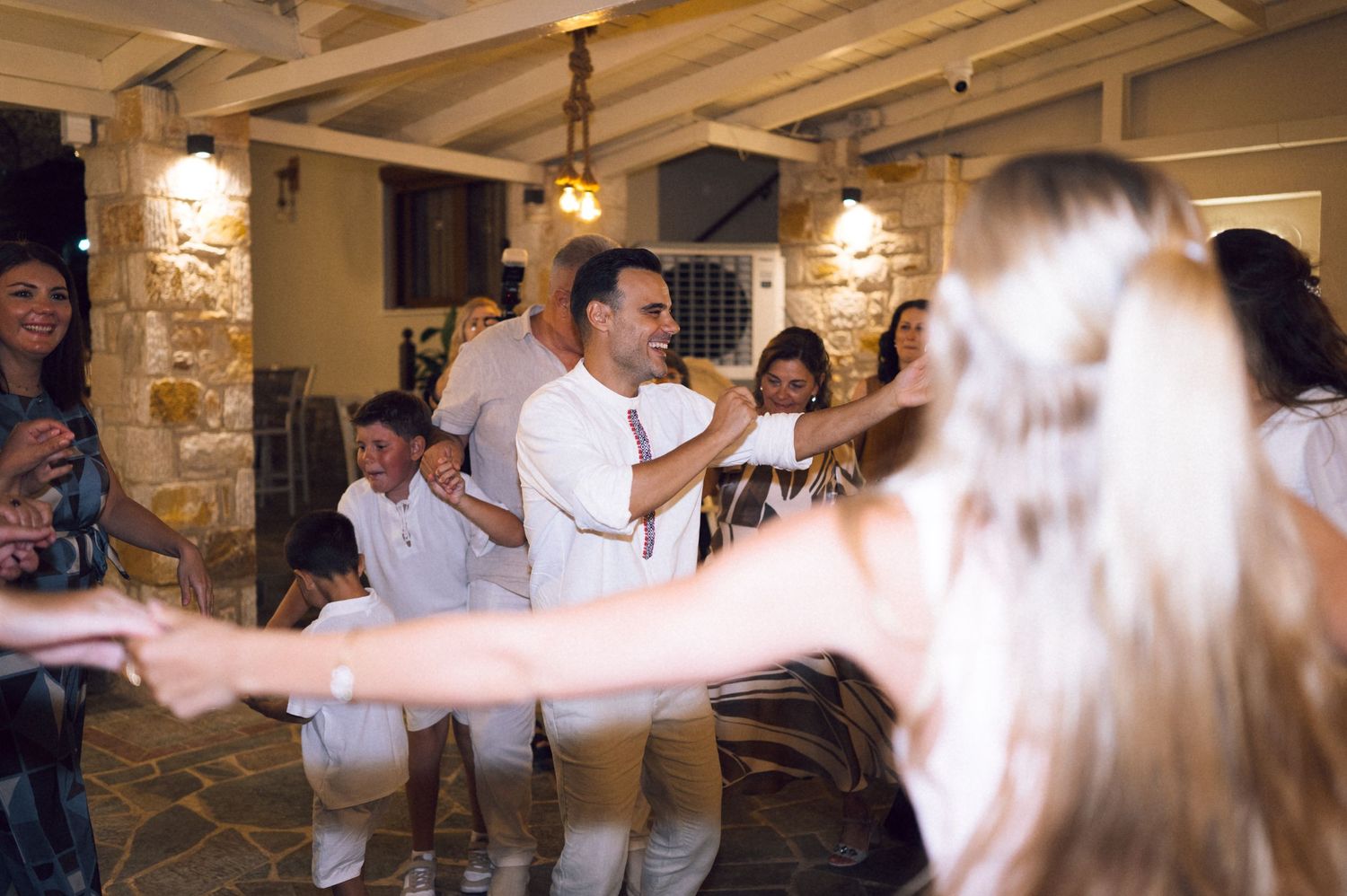 People dancing joyfully at a lively indoor party or wedding celebration in a rustic stone venue.