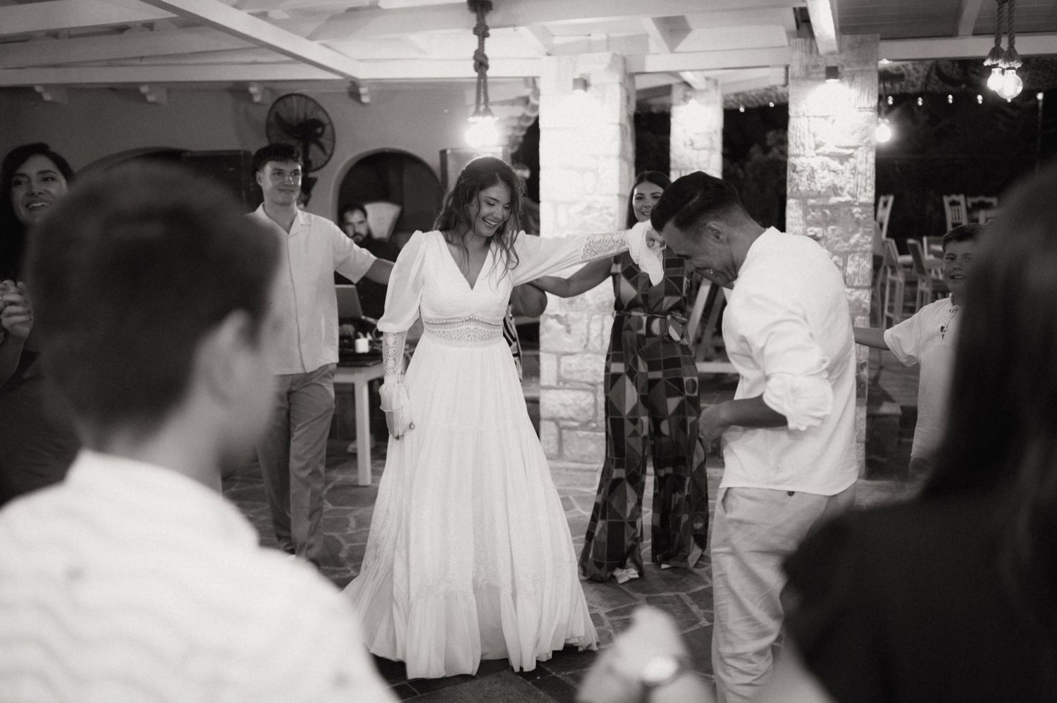 Black and white photo of a bride in a white gown dancing with a guest at an elegant wedding reception.