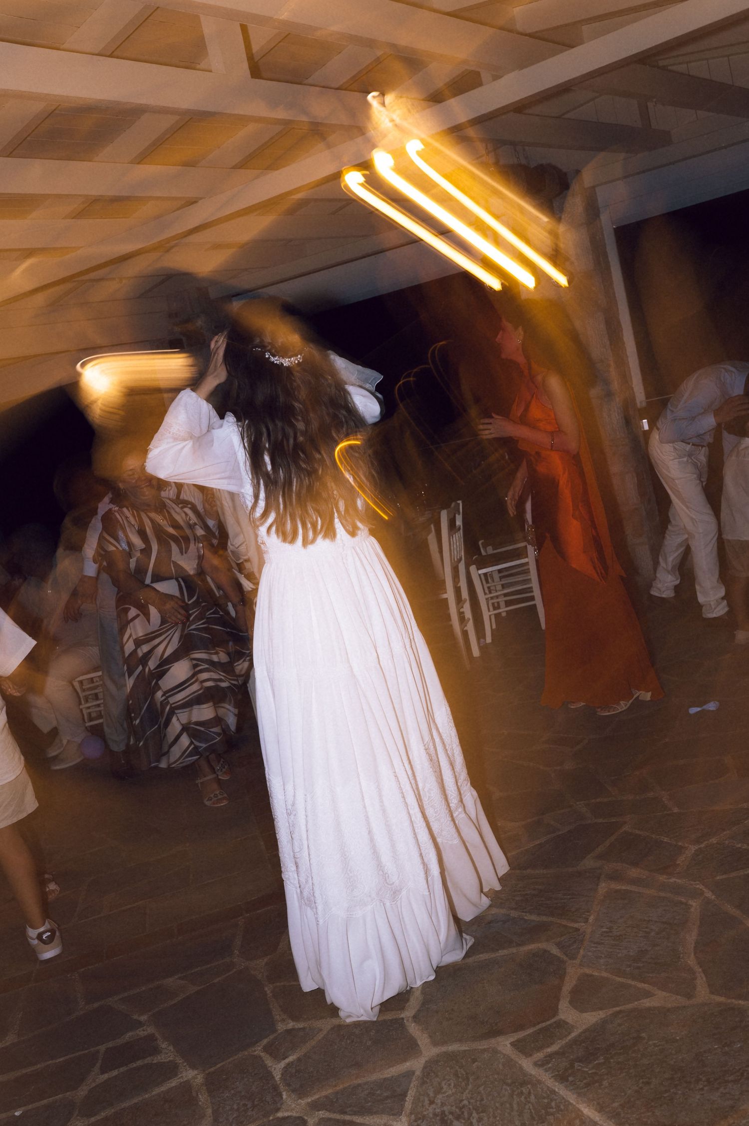 Bride in white flowing gown dancing at wedding reception under warm neon lights on stone floor.