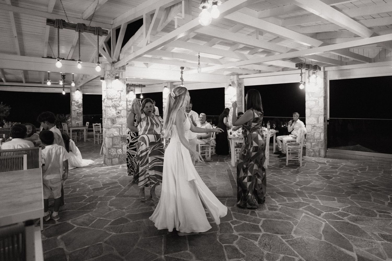 Bride dancing with guests at an outdoor wedding reception under string lights on a stone patio.