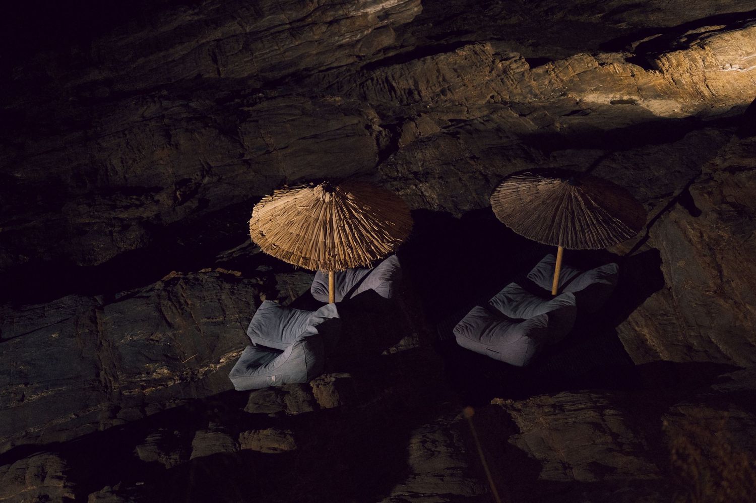 Two straw parasols rest on rocky cave ledges in a dark cavern, illuminated by dim light.