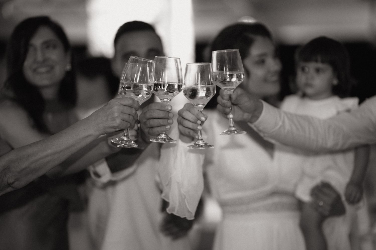 Black and white photo of people clinking wine glasses in a celebratory toast at a wedding reception.