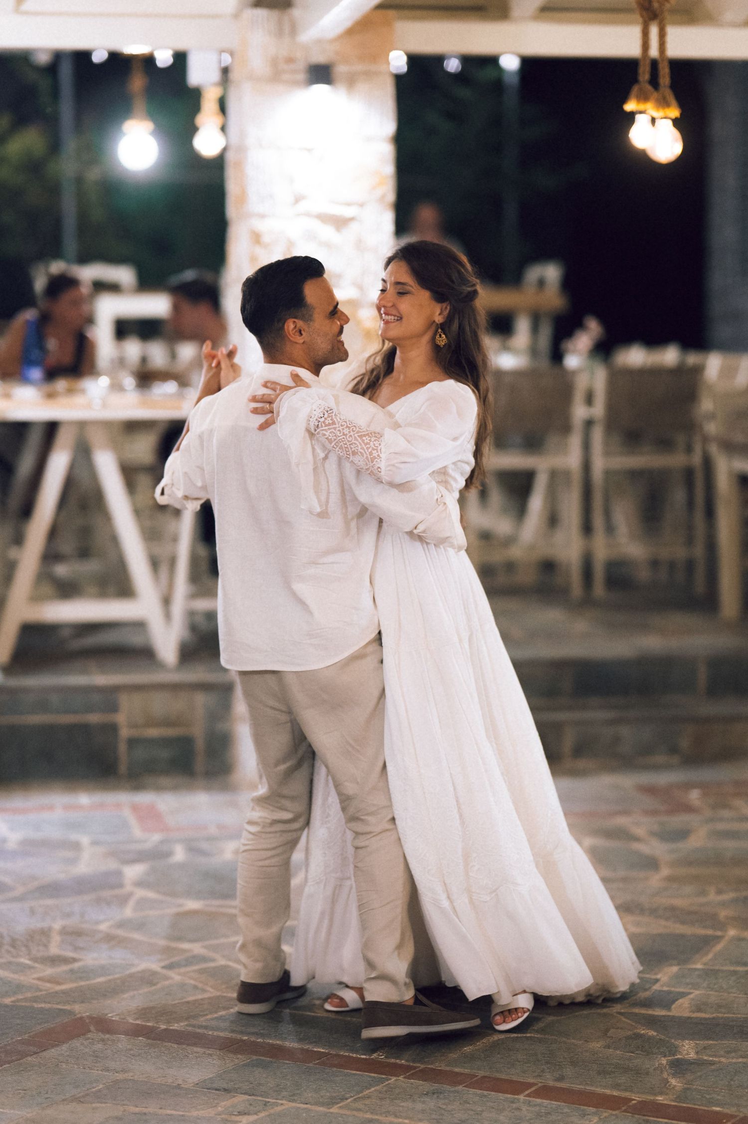 Couple sharing their first dance at an outdoor wedding reception, bride in white gown, groom in white shirt.