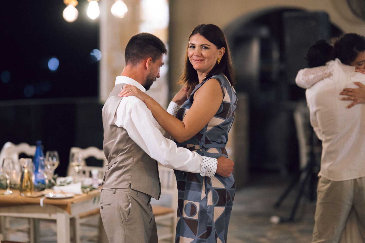 Couple dancing elegantly at an outdoor evening wedding reception with guests and decorated tables in background.