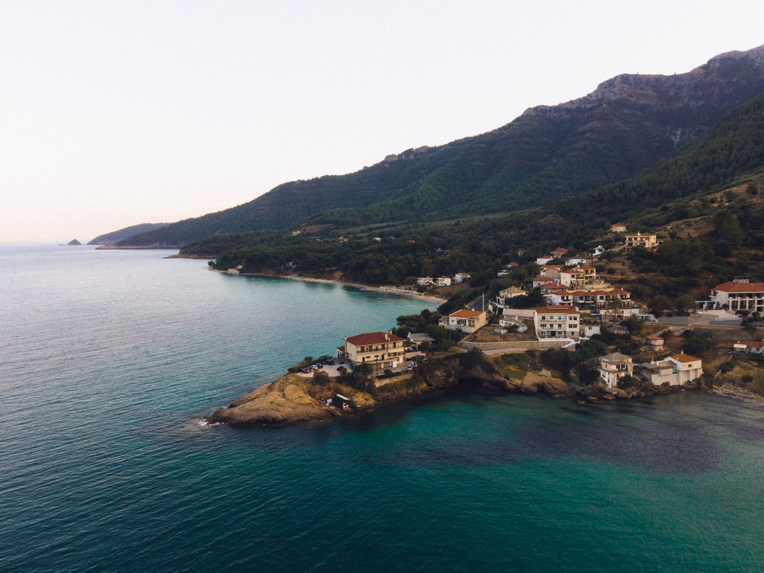Aerial view of a small coastal village with turquoise waters and lush green mountains in the background.