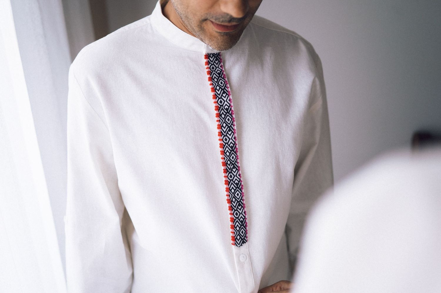 Man wearing a white kurta with red and blue embroidered trim detail on the front placket.
