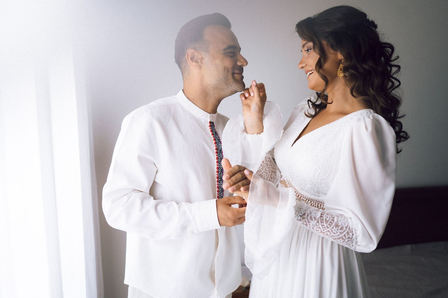 Couple in white outfits sharing a romantic moment, man in white shirt and tie, woman in elegant white dress.