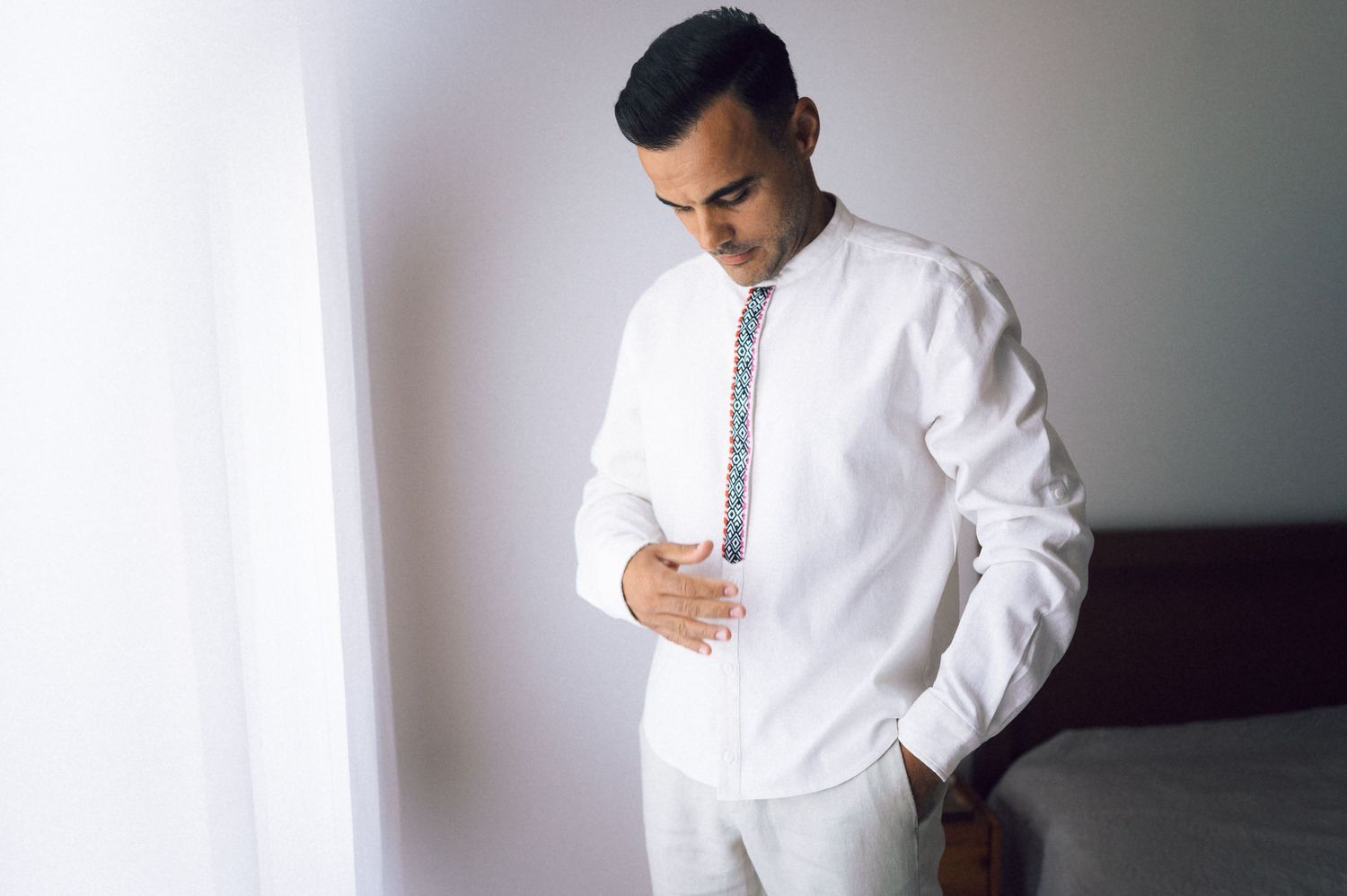 Man in white embroidered shirt adjusting his outfit while getting ready for a wedding ceremony.